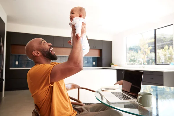 미소짓기 머물면서 아프리카계 미국인 아버지는 집에서 노트북 컴퓨터로 일하는 아기를 — 스톡 사진