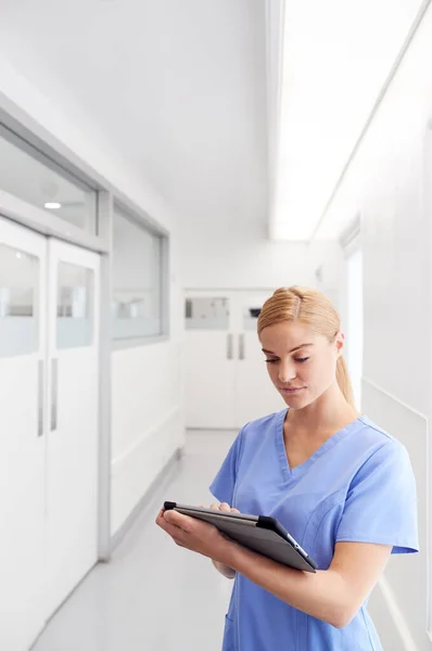 病院の廊下でデジタルタブレットを使用してスクラブを身に着けている女性医師 — ストック写真