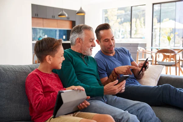 多代男性西班牙裔家庭坐在沙发上 使用手机和数字平板电脑 — 图库照片