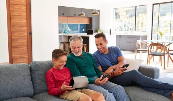 携帯電話やデジタルタブレットを使用して自宅でソファに座っている世代の男性ヒスパニック系家族 — ストック写真