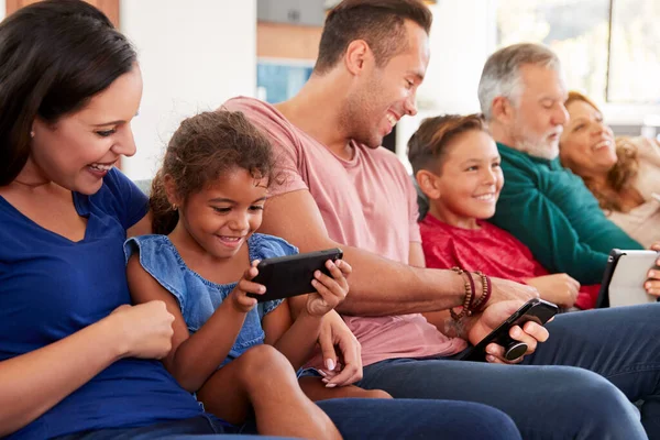 ソファでテレビを見て デジタルタブレットや携帯電話で遊んでいる世代の家族 — ストック写真