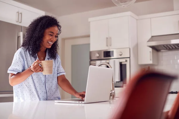 自宅からノートパソコンでキッチンに立つパジャマ姿の女性 — ストック写真