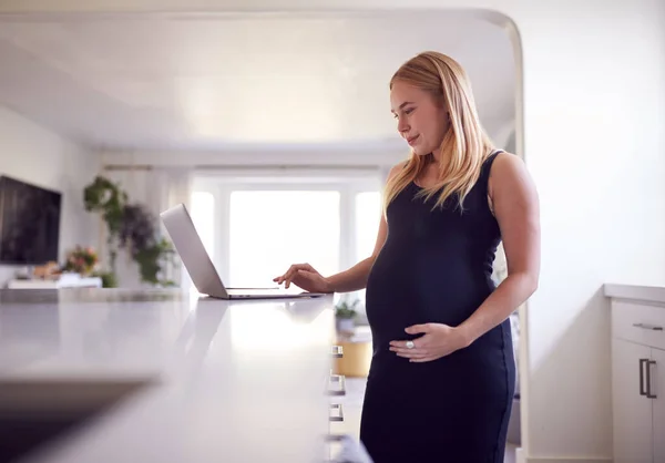 孕妇站在厨房柜台旁 在笔记本电脑上做家务 — 图库照片