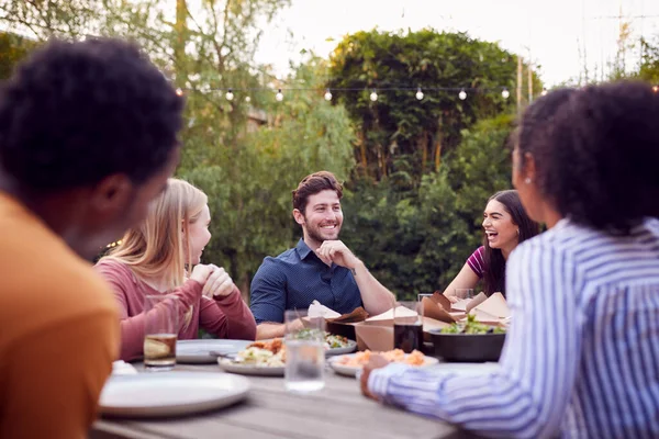 夏のガーデンパーティーで食事を楽しむテーブルに座っている多文化の友人 — ストック写真