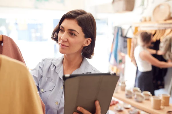 ファッションストアの女性オーナーは デジタルタブレットを使用して衣料品店でレールをチェックする — ストック写真