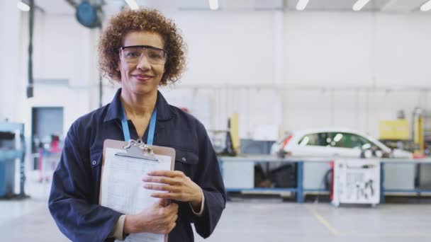 戴安全眼镜的女导师拿着剪贴板在大学教汽车机械学徒 慢镜头对着镜头笑的肖像 — 图库视频影像