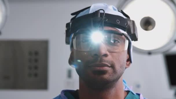 Hastanenin Ameliyathanesinde Kameraya Koruyucu Gözlüklü Baş Meşaleli Erkek Cerrahın Portresi — Stok video