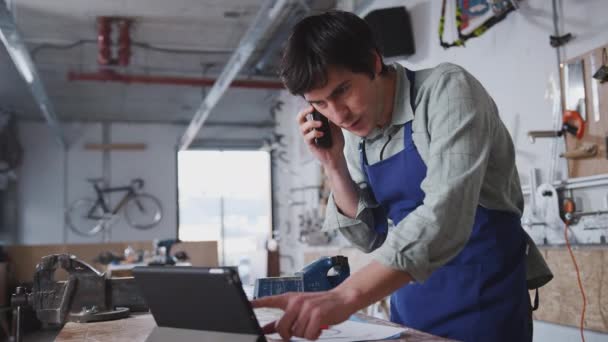 Männlicher Geschäftsinhaber Werkstatt Nutzt Digitales Tablet Und Telefoniert Mit Handy — Stockvideo