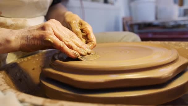 陶芸スタジオの陶磁器ホイールにクレイプレートにデザインを入れる男性ポッターのクローズアップ — ストック動画