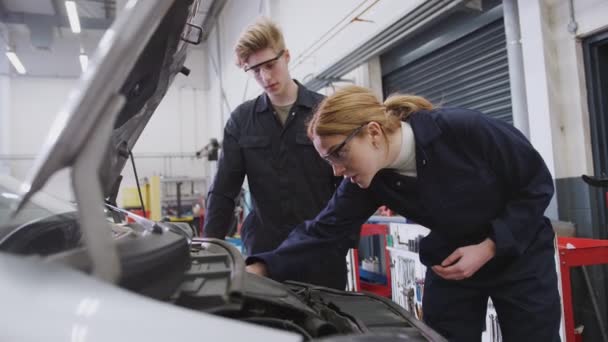 男性と女性の学生研究大学で自動車整備士の見習い車のエンジンを見て スローモーションで撮影 — ストック動画
