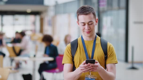 Glimlachende Mannelijke Student Controleert Mobiele Telefoon Drukke Gemeenschappelijke Campus Gebouw — Stockvideo