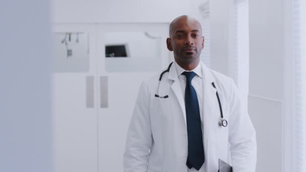 病院の廊下に白いコートを着て聴診器を持つ男性医師の肖像クリップボードを保持 スローモーションで撮影 — ストック動画