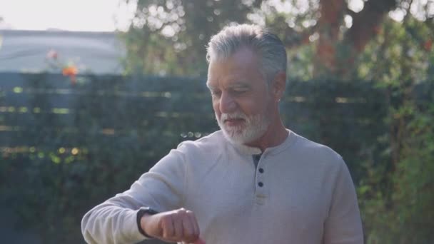 Senior Ισπανόφωνος Άνθρωπος Κοιτάζοντας Έξυπνο Ρολόι Στον Κήπο Στο Σπίτι — Αρχείο Βίντεο
