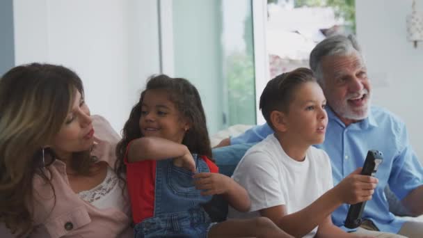 与孙子孙女一起坐在沙发上看电视的西班牙裔祖父母和孙子孙女们一起在家里放松 动作缓慢 — 图库视频影像