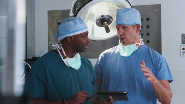 Dwóch Chirurgów Fartuchu Dyskutujących Nad Tabletem Cyfrowym Szpitalnym Teatrze Operacyjnym — Wideo stockowe