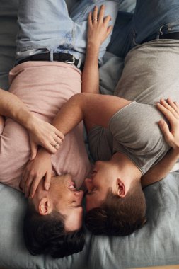 Overhead Shot Of Loving Same Sex Male Couple Lying On Bed At Home Hugging Together clipart