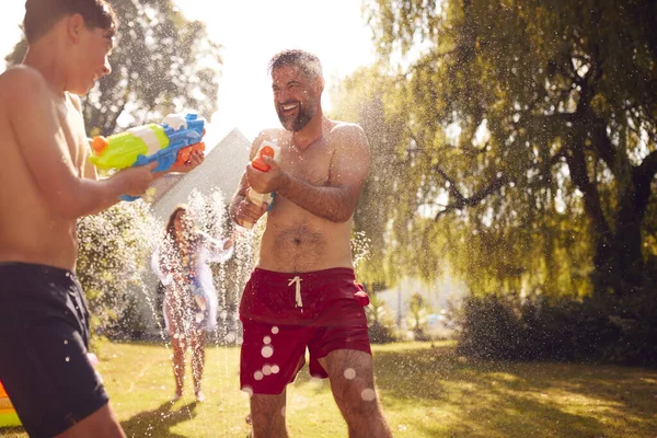 夏の庭で水ピストルで水と戦う水着を着た家族 — ストック写真