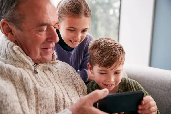 Внуки Диване Дома Показывают Дедушке Пользоваться Мобильным Телефоном — стоковое фото