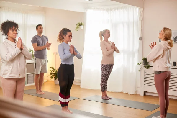 Group With Teacher Standing And Meditating In Yoga Class Inside Community Center