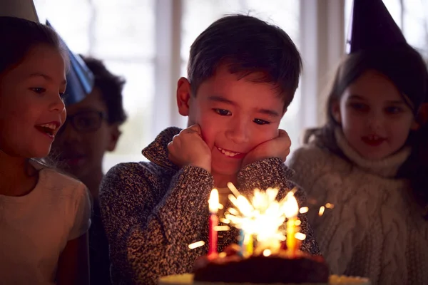 自宅で友人のグループと一緒に誕生日を祝う少年は スパークラーで飾られたケーキを与えられています — ストック写真