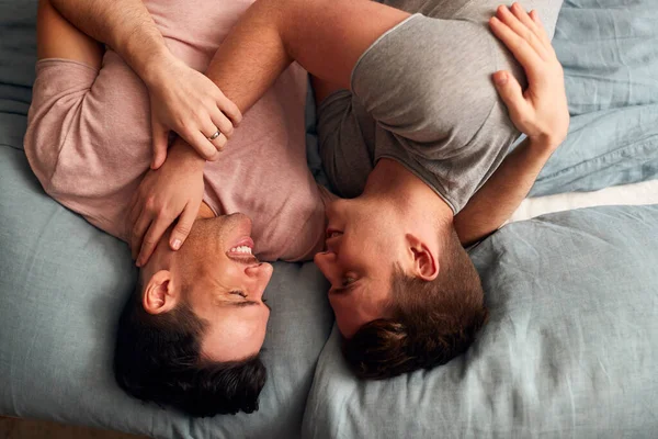 Overhead Shot Of Loving Same Sex Male Couple Lying On Bed At Home Hugging Together