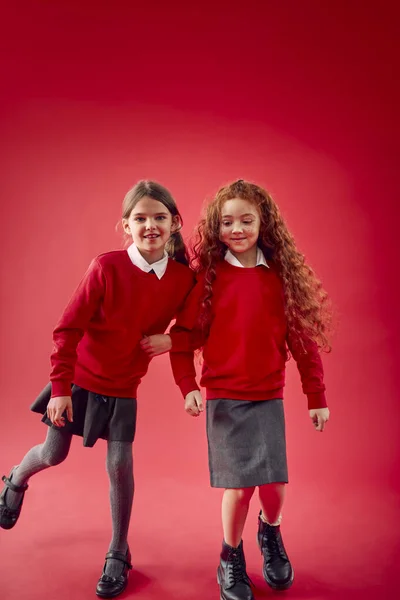 Twee Basisschoolleerlingen Dragen Uniforme Koppelarmen Tegen Achtergrond Van Red Studio — Stockfoto