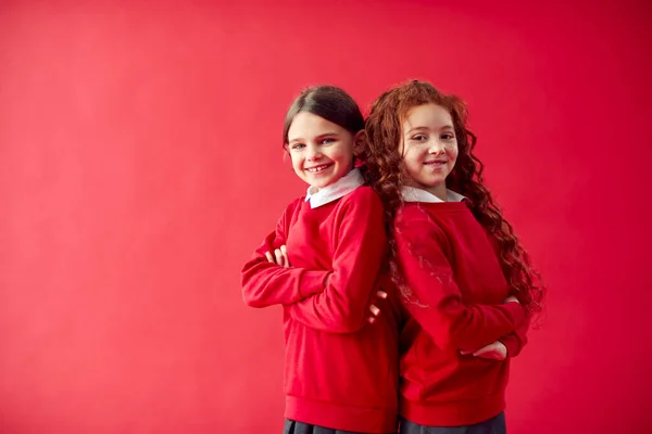 制服を着た2人の小学生が赤いスタジオの背景に背を向ける — ストック写真