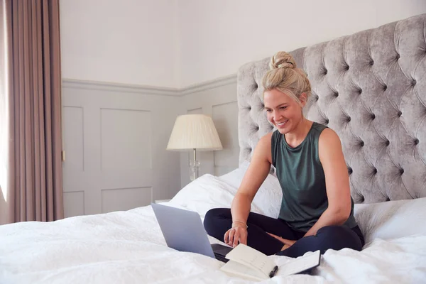 流行のロックダウン中にビデオ通話で自宅から働くラップトップでベッドに座っているビジネスマンの女性 — ストック写真