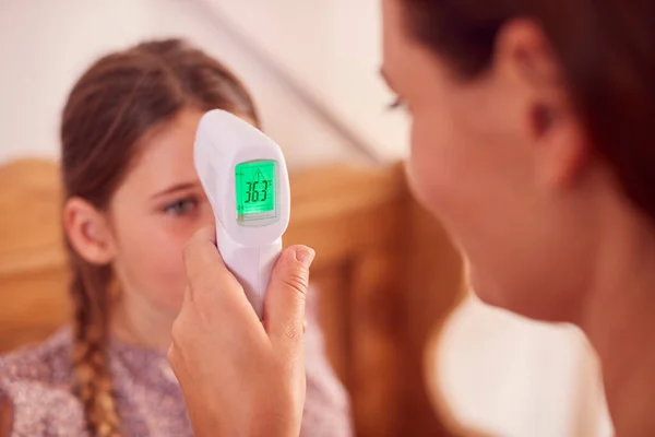 用非接触式数字式温度计密切检查母亲在家中检查女儿的体温 — 图库照片