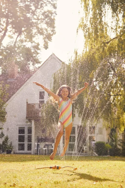 穿着泳衣在夏日花园玩水的女孩从花园洒水 — 图库照片