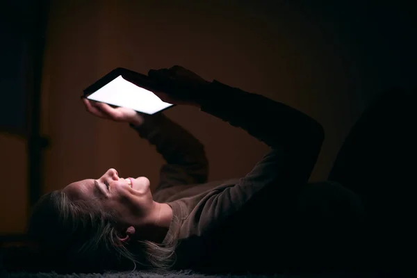 Glimlachende Vrouw Met Gezicht Verlicht Door Digitale Tablet Scherm Liggen — Stockfoto