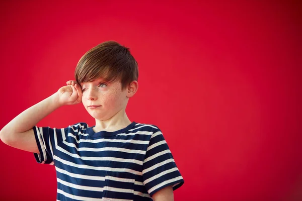 赤いスタジオの背景に目をこすり疲れた少年の肖像画 — ストック写真