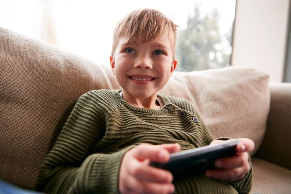 年轻男孩在家沙发上玩手机游戏玩得很开心 — 图库照片