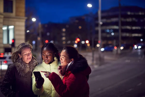 夜の街で女性の友達のグループ携帯電話アプリを使用してタクシーを注文 — ストック写真