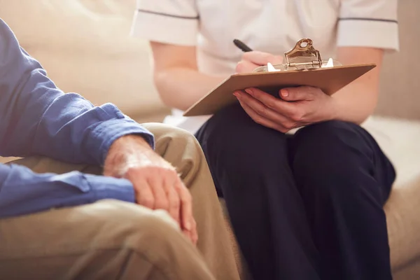 Zbliżenie Kobieta Lekarz Robi Notatki Podczas Domu Wizyta Dla Senior — Zdjęcie stockowe