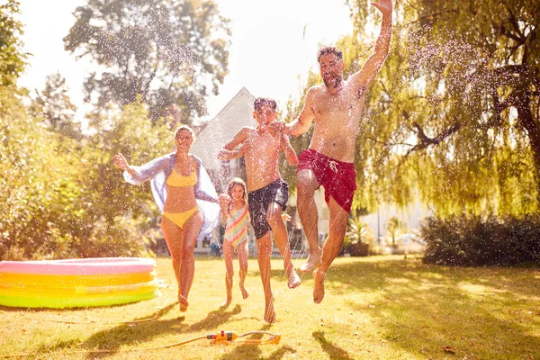 Family Running Water Garden Sprinkler Having Fun Wearing Swimming Costumes — Stock Photo, Image