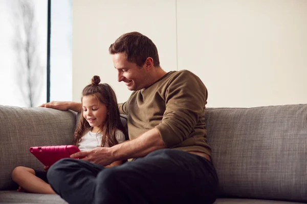 爸爸和女儿坐在沙发上在家一起玩数字桌面上的粉盒 — 图库照片