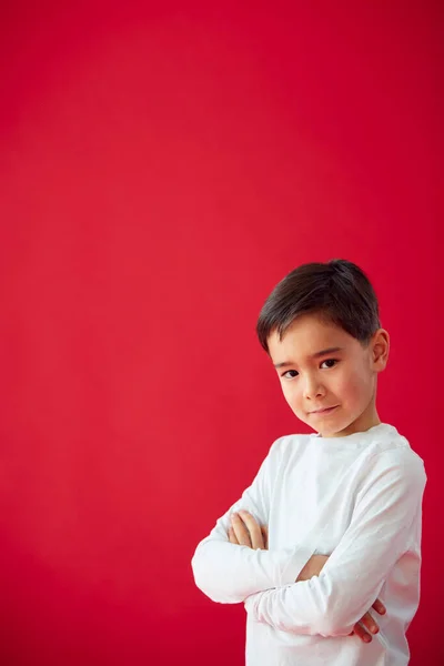 带着折叠式臂膀的小男孩在红色工作室背景下的肖像在相机前微笑 — 图库照片