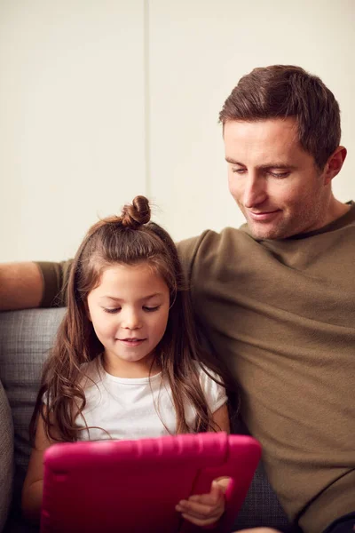 自宅でソファに座っている父と娘が自宅でピンクのケースでデジタルタブレットで一緒にプレイ — ストック写真