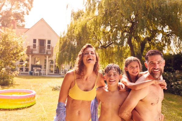 庭のスプリンクラーから水で遊ぶ楽しさを持つ水着を身に着けている家族の肖像 — ストック写真