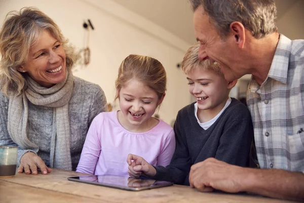 祖父母と一緒に自宅でデジタルタブレットで遊んでいる孫たち — ストック写真