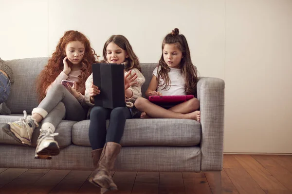 与朋友坐在沙发上的一群女孩在家里玩数字桌球和手机 — 图库照片