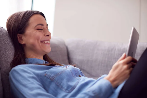 Skrattar Ung Kvinna Hemma Liggande Soffan Tittar Digital Tablett — Stockfoto