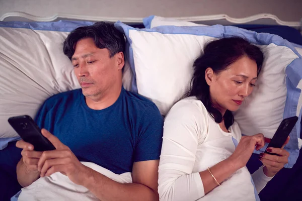 Mature Couple Wearing Pyjamas Addicted Using Mobile Phones Lying Bed — Stock Photo, Image