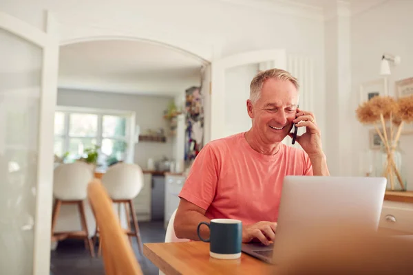 Hombre Retirado Teléfono Casa Cocina Usando Ordenador Portátil — Foto de Stock