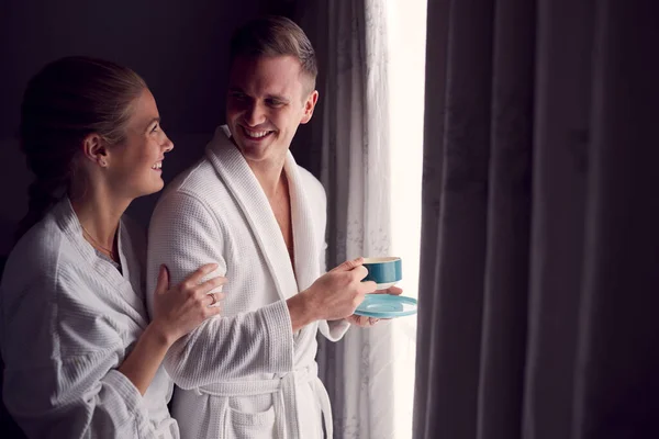 ロマンチックなホテルやスパでバスローブを着たカップルが熱い飲み物でカーテンを開けることで立ち上がる休憩 — ストック写真