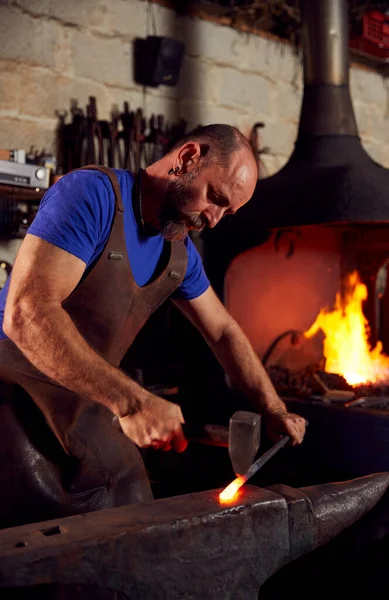 Blazing Forgeを背景にしたAnvilでの男性鍛冶屋の金属加工 — ストック写真