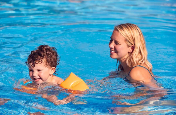 户外游泳池里的母子暑期教子带着受宠若惊的臂章游泳 — 图库照片