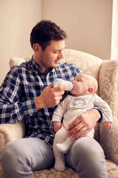 Vater Füttert Baby Sohn Mit Flasche Auf Stuhl Wohnzimmer — Stockfoto