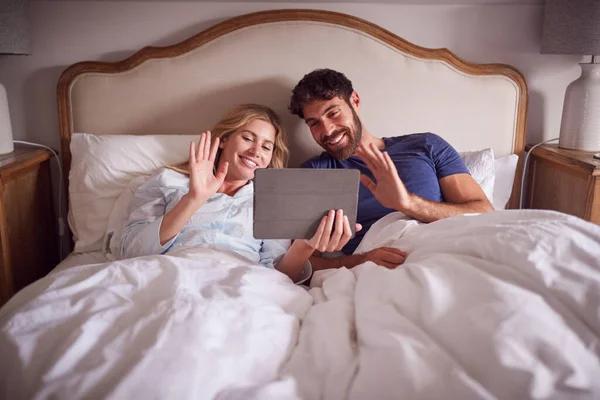 デジタルタブレットでビデオ通話を持つ朝のベッドで寝そべっているカップル — ストック写真